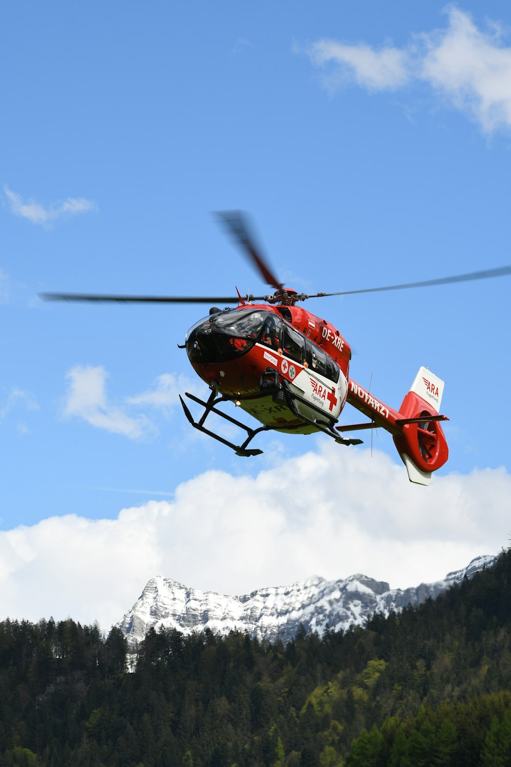 red and black helicopter flying over snow covered mountain during daytime