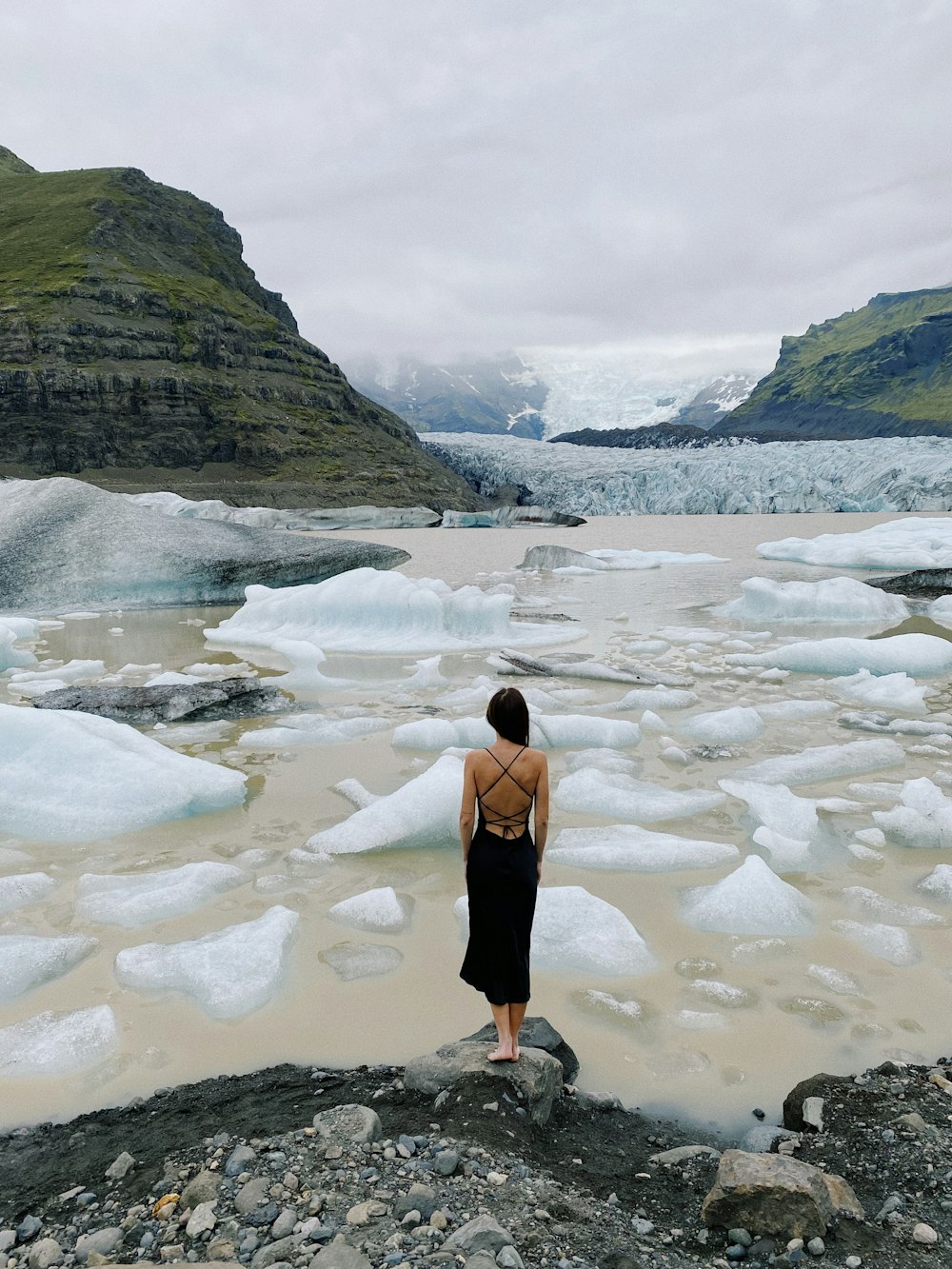 woman in black tank top and black skirt standing on rocky shore during daytime