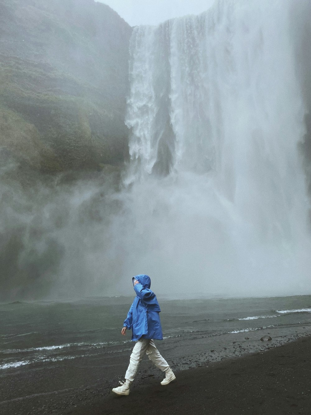 person in blue hoodie standing on seashore during daytime