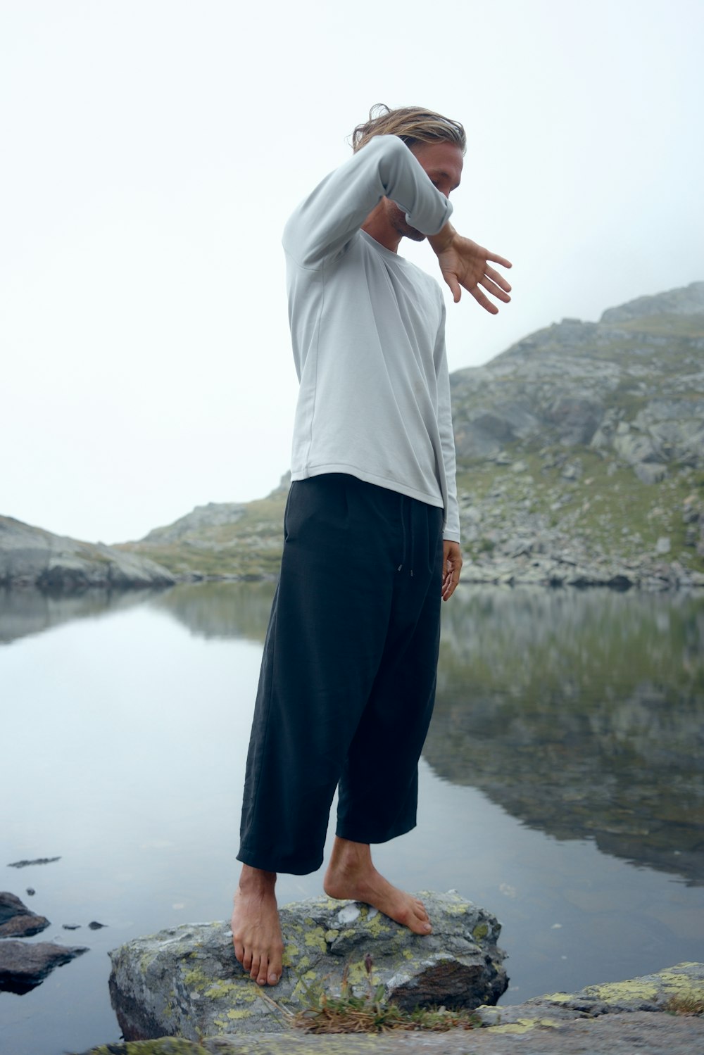 man in white shirt and black pants standing near lake during daytime