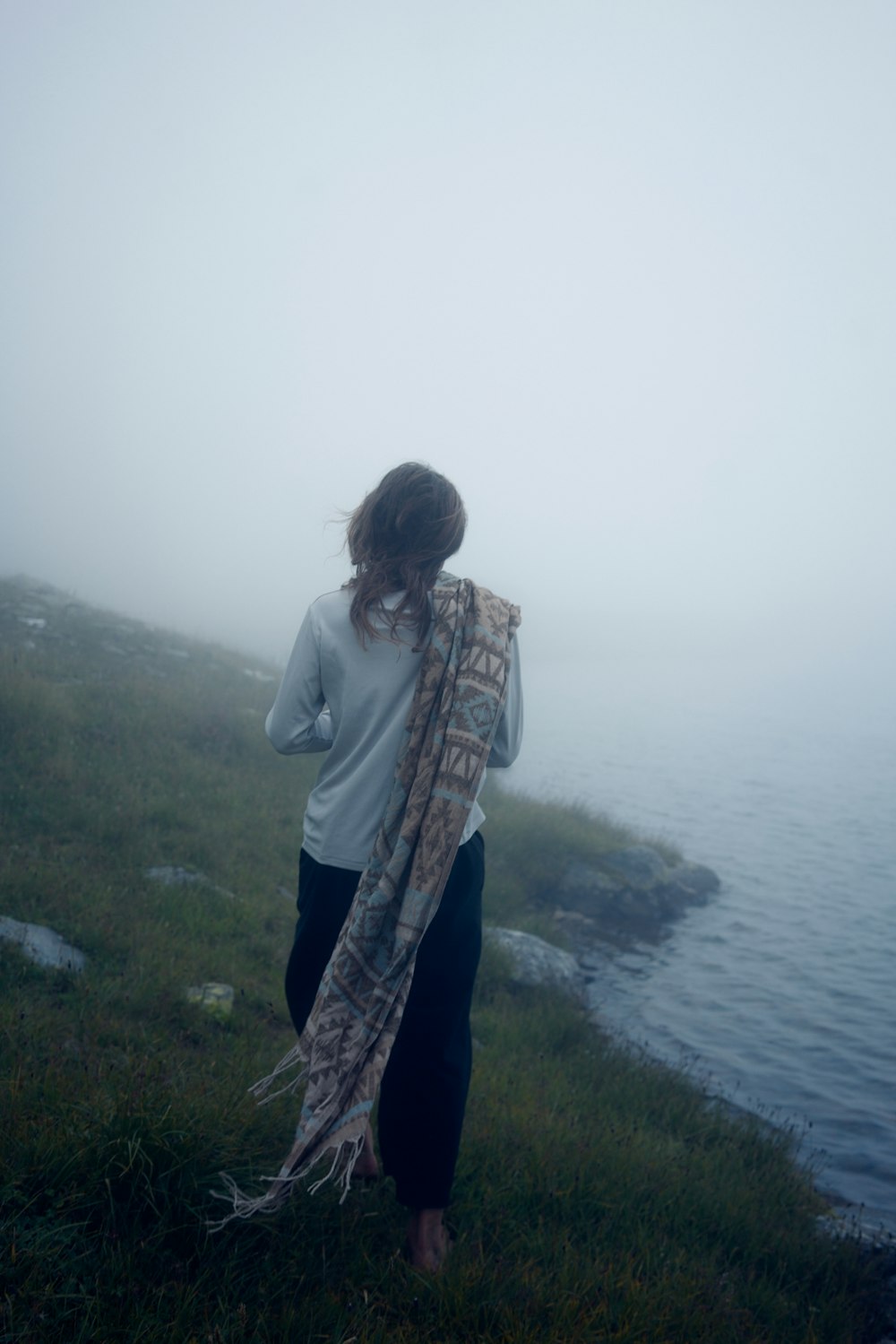 woman in gray jacket standing on green grass field near body of water during daytime