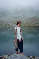 woman in white long sleeve shirt and black pants standing near lake during daytime