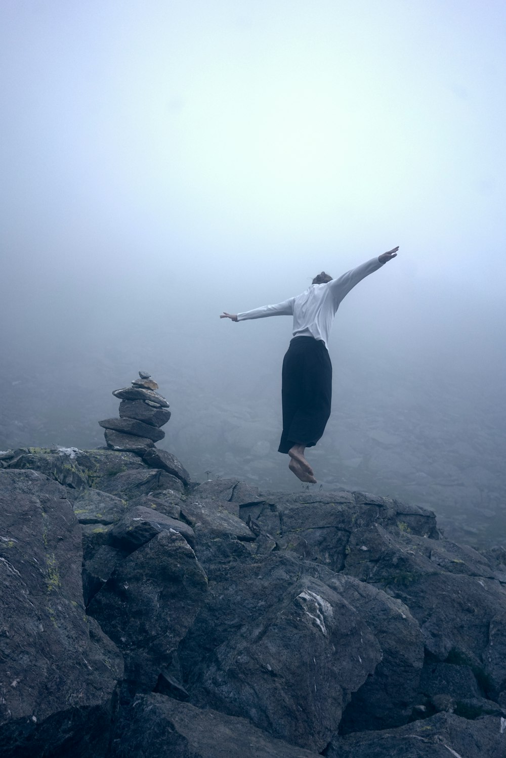 woman in white long sleeve shirt and black pants standing on rock