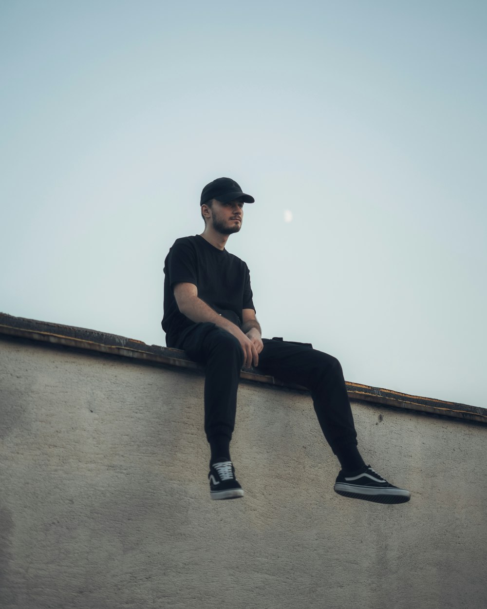 man in black shirt and black pants sitting on concrete wall