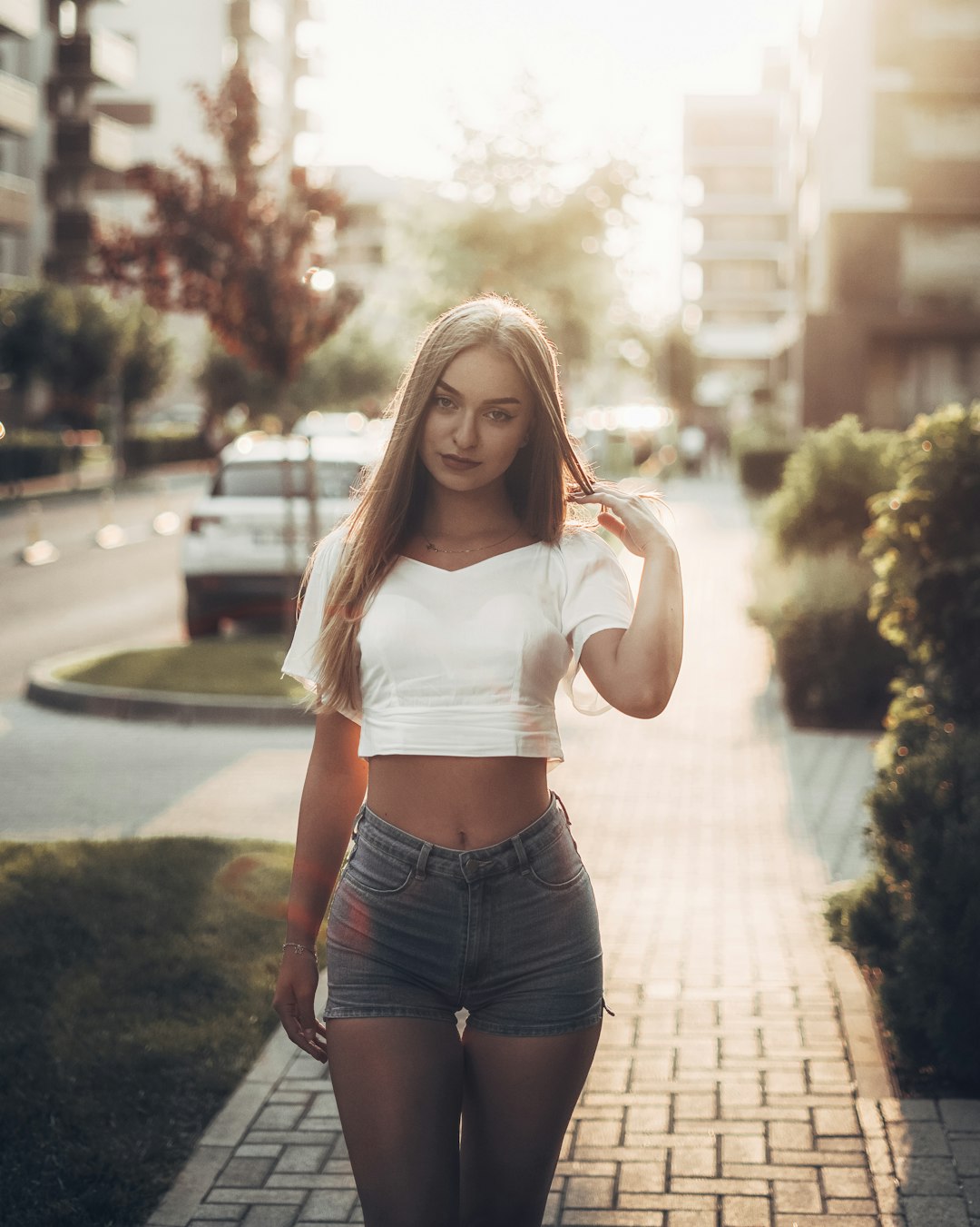 woman in white tank top and blue denim shorts standing on gray concrete pathway during daytime