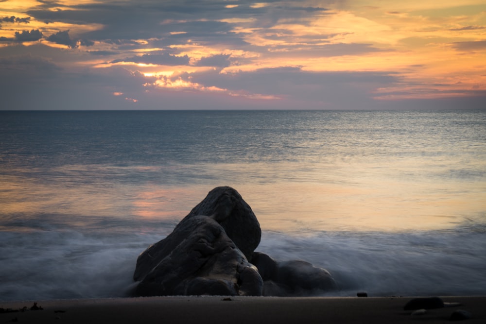 black rocks on sea shore during sunset