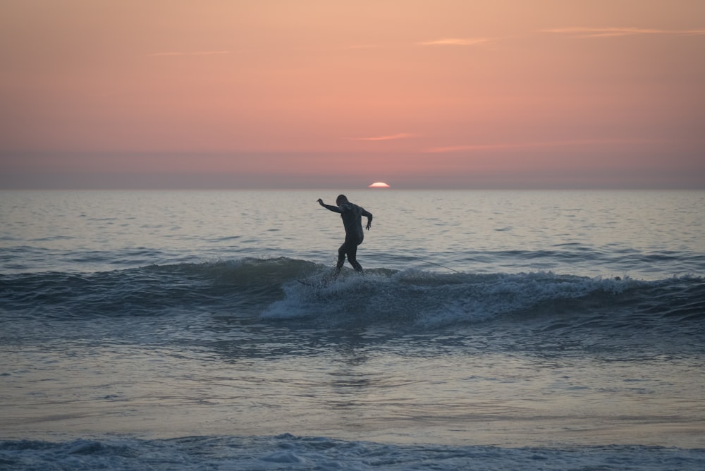 uomo in muta nera che fa surf sulle onde del mare durante il giorno