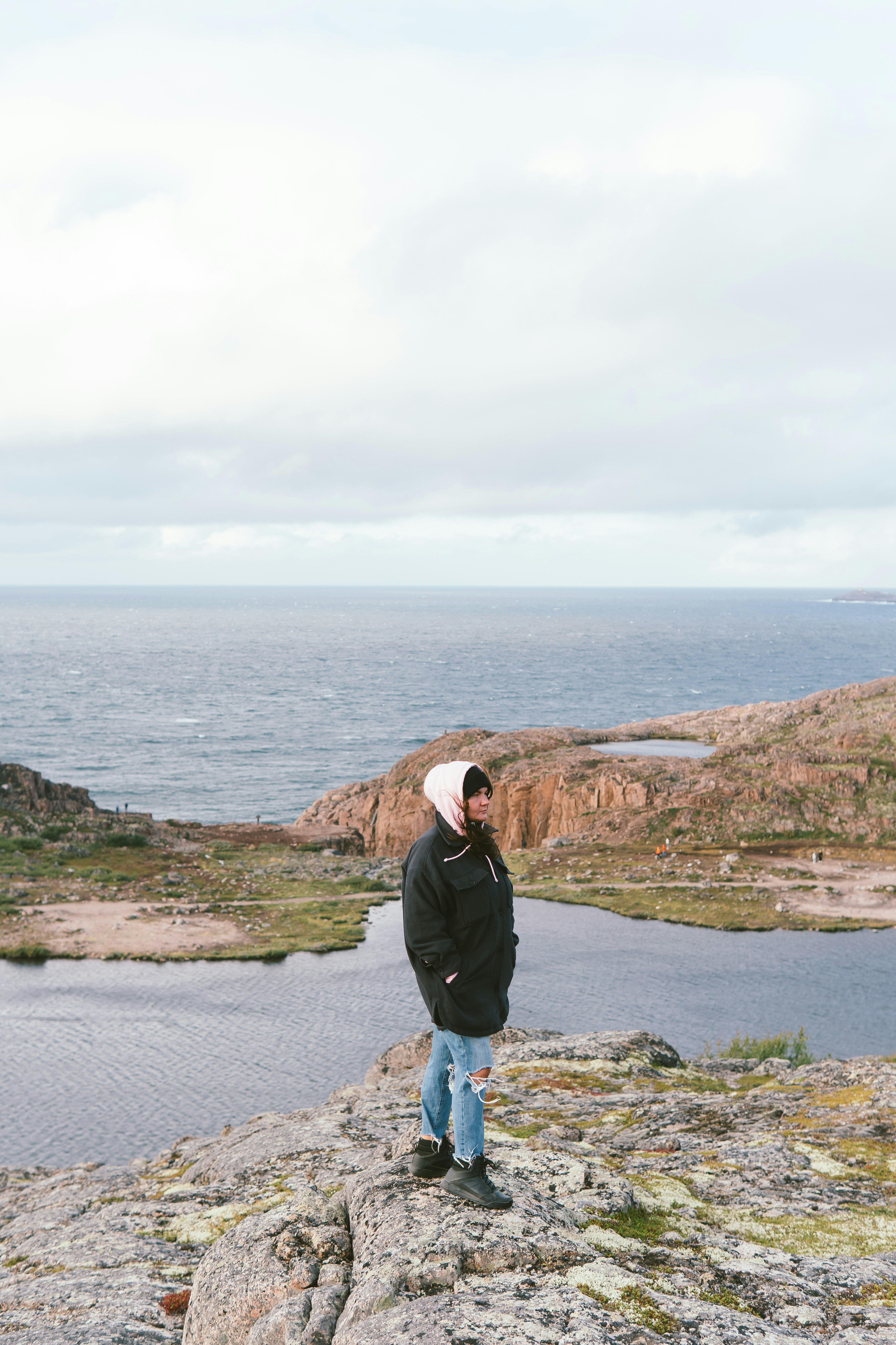 man in black jacket standing on gray rock near body of water during daytime