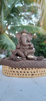 An eco-friendly clay Ganesh idol resting on a bed of fresh green leaves.