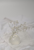 Delicate white flowers in a simple glass vase on a linen-covered table.