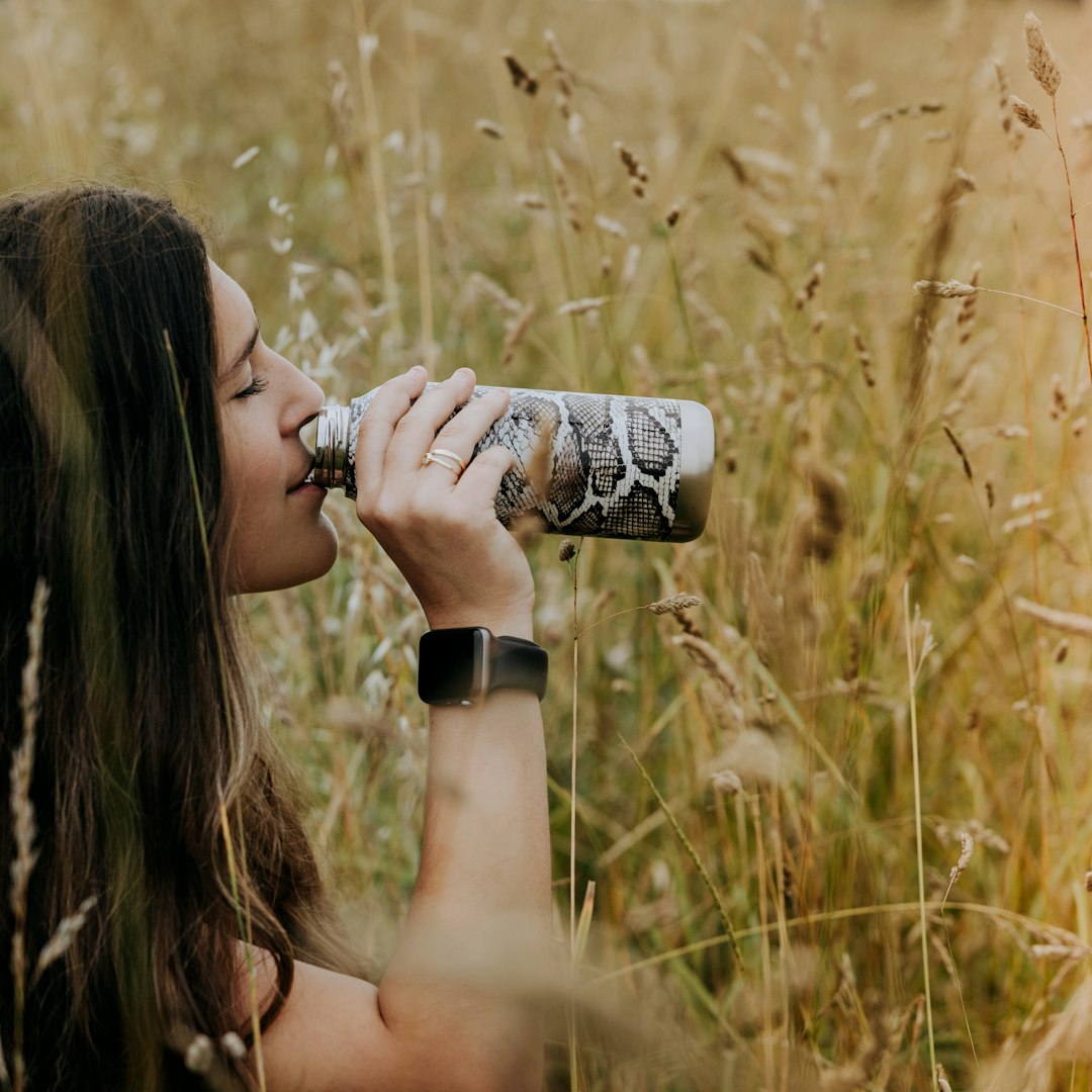 woman drinking on can on brown grass field during daytime