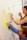 Two people are using sticky notes on a wall for organizing tasks or ideas. One person is writing on a note while the other observes with interest, holding a beverage can. The scene suggests collaborative planning or brainstorming.