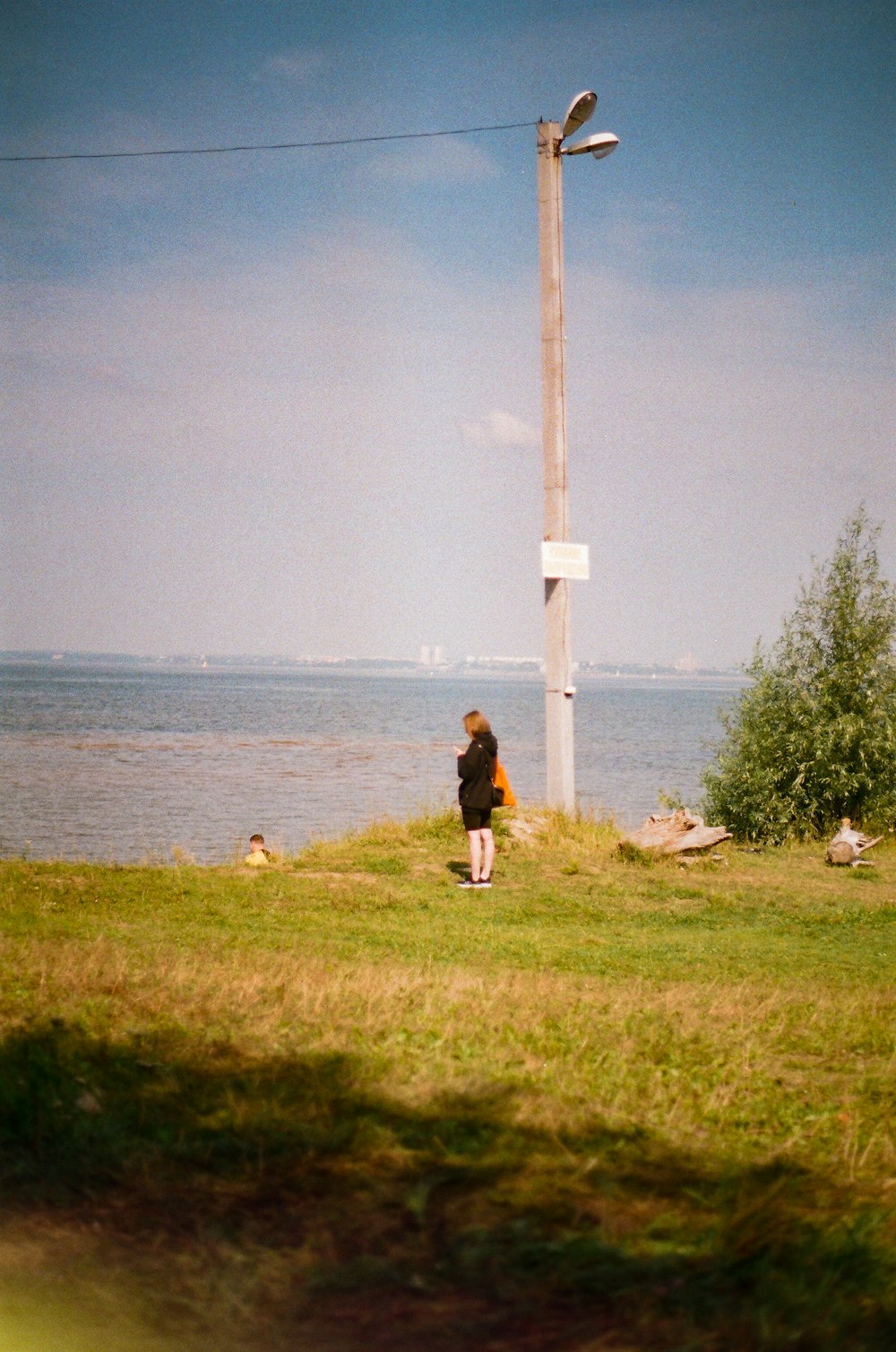 person in black jacket standing on green grass field near body of water during daytime