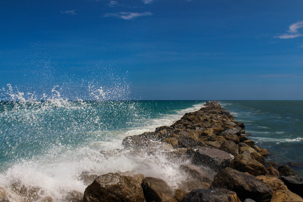 ocean waves crashing on rocks under blue sky during daytime