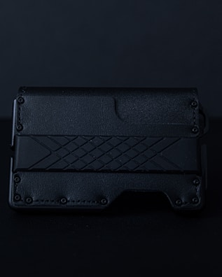 A sleek, textured black wallet featuring a geometric pattern on its surface. The material appears to be leather or a leather-like synthetic, with a rugged, stylish design.