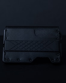 A sleek, textured black wallet featuring a geometric pattern on its surface. The material appears to be leather or a leather-like synthetic, with a rugged, stylish design.