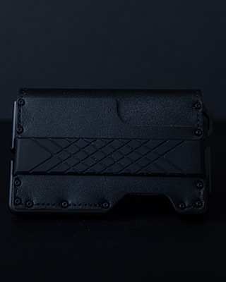 A sleek, textured black wallet featuring a geometric pattern on its surface. The material appears to be leather or a leather-like synthetic, with a rugged, stylish design.