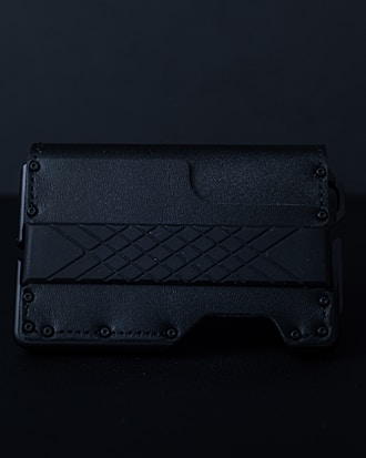 A sleek, textured black wallet featuring a geometric pattern on its surface. The material appears to be leather or a leather-like synthetic, with a rugged, stylish design.