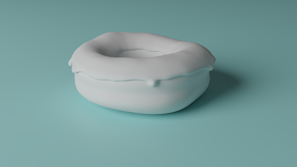 A soft, cushion-like object with a rounded, pillow-like shape is placed on a smooth, teal-colored surface. The object appears plush and somewhat irregular in form, suggesting a comfortable, inviting texture.