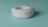 A soft, cushion-like object with a rounded, pillow-like shape is placed on a smooth, teal-colored surface. The object appears plush and somewhat irregular in form, suggesting a comfortable, inviting texture.