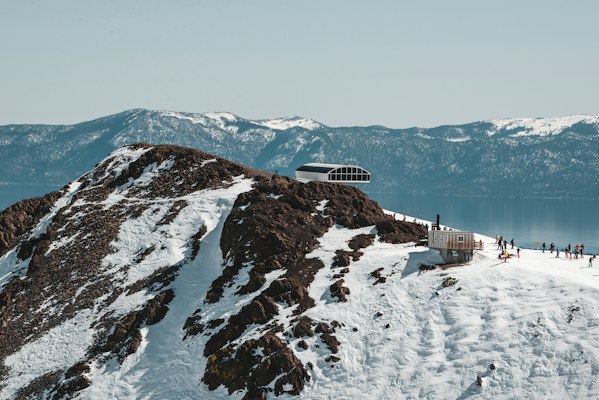 The High Camp ridge at Palisades Tahoe with its round-roofed building and Lake Tahoe and the snowy far shore behind