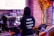 A person wearing a black hoodie with hashtags like #ORGANIC, #PLANTBASED, #SMOOTHIEBOWL, and #YUMMY stands at an espresso machine making a coffee. The background includes a menu, a wall with an autumn-themed decoration, and various equipment like a cash register.