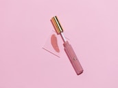 Glossy pink and emerald lip gloss swatches on a white background reflecting light.