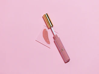 Close-up of a glossy lip oil dripping softly on a pastel pink background with subtle light reflections.