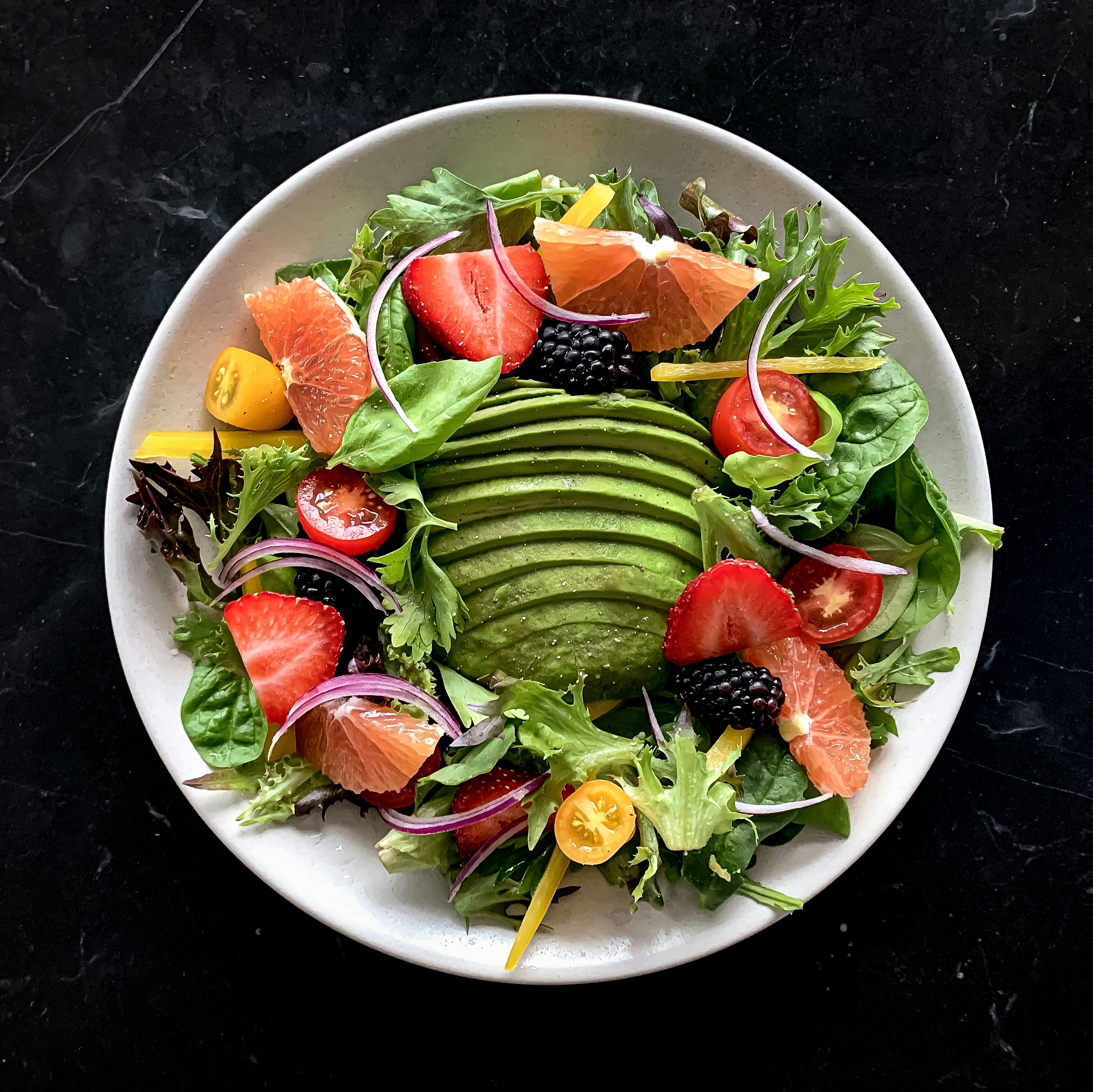 Ensalada colorida con vegetales frescos, aguacate y aderezo, fondo oscuro minimalista