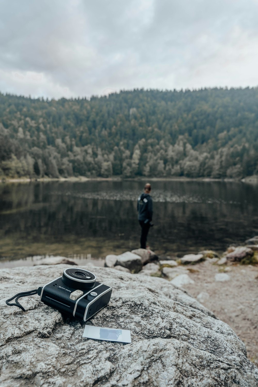 man in black jacket standing on rock near lake during daytime