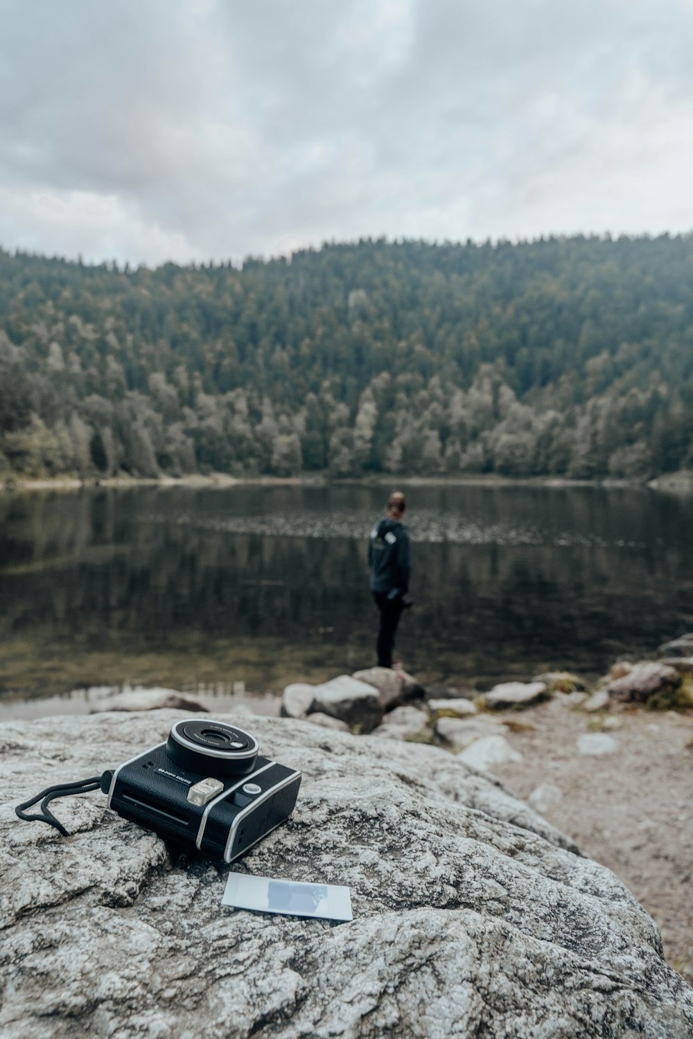 uomo in giacca nera in piedi sulla roccia vicino al lago durante il giorno