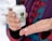 A person holds a bottle of CBD body lotion with the label '1000 MG CBD, Eden's CBD, 100% Pure CBD' and dispenses a small amount onto their palm. The person is wearing a colorful, patterned fabric in the background.