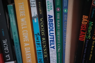 A collection of books arranged vertically on a shelf, featuring a variety of titles and colors on their spines.