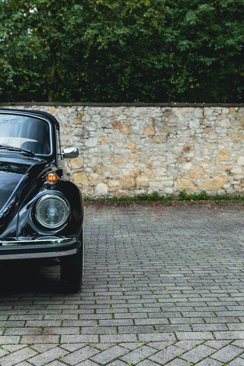 black volkswagen beetle parked beside brown brick wall