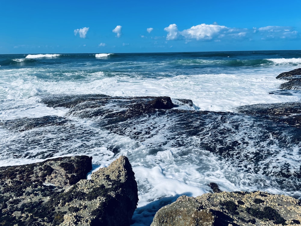 ocean waves crashing on rocks under blue sky during daytime