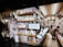 A bookstore aisle filled with shelves stocked with brightly colored manga volumes. A person browses the shelves on the right side, while another person is partially visible holding a phone. A cartoon rabbit character holding a book with a QR code invites readers to access free manga online.