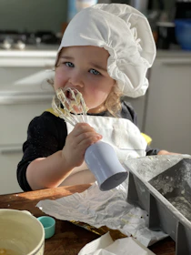 a little girl wearing a chef's hat and holding a whisk