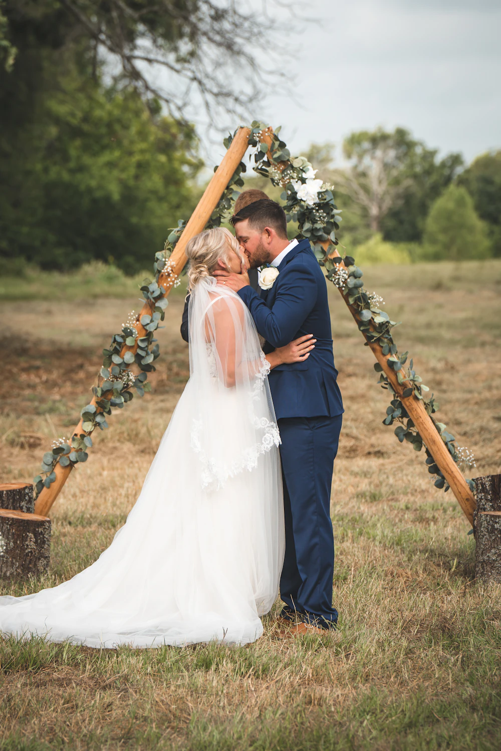 Bride and groom kissing beneath a floral arch at an outdoor garden ceremony