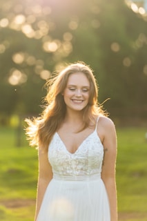 A stylish woman wearing a flowing white dress in a sunlit park.