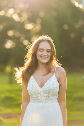 A model wearing a flowing bohemian dress in soft beige and cream tones, standing in natural sunlight