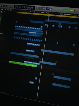 A digital audio workstation interface displaying a timeline with various tracks. Blue and green colored bars represent different audio elements, indicating a complex music project in progress. The interface includes time markers, labels, and controls for editing sound files.