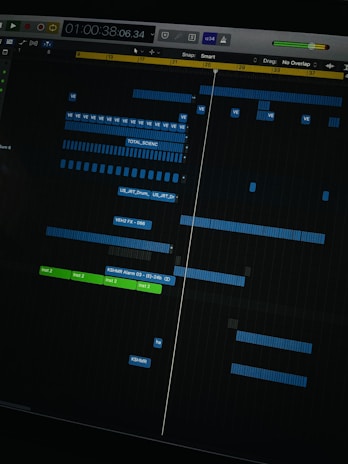 A digital audio workstation interface displaying a timeline with various tracks. Blue and green colored bars represent different audio elements, indicating a complex music project in progress. The interface includes time markers, labels, and controls for editing sound files.