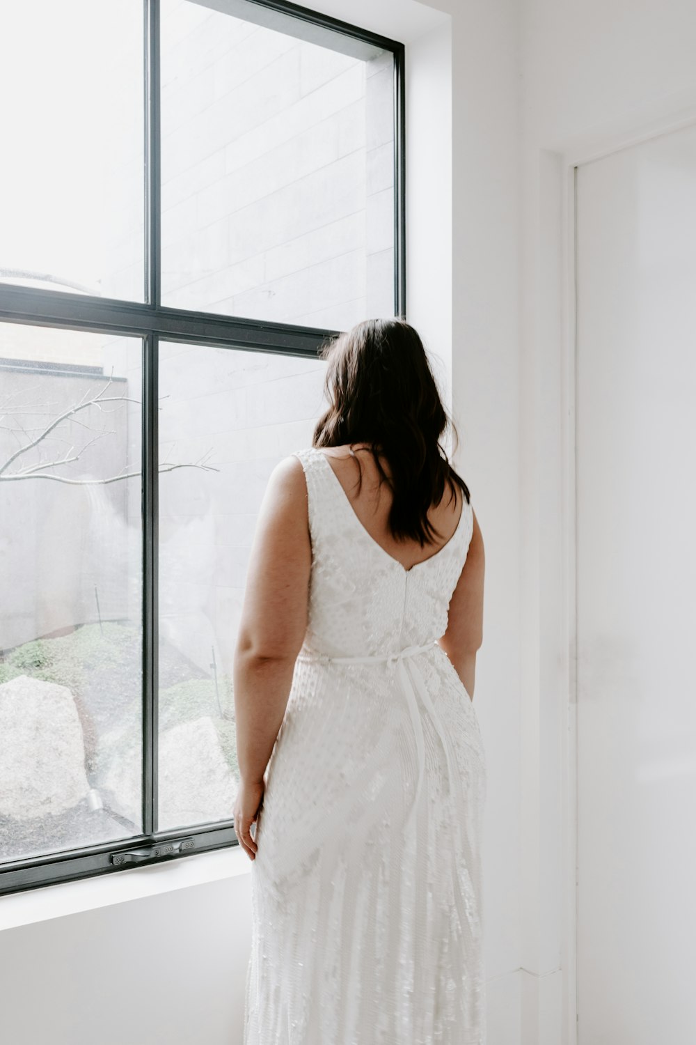 창문 근처에 서 있는 흰색 민소매 드레스를 입은 여자