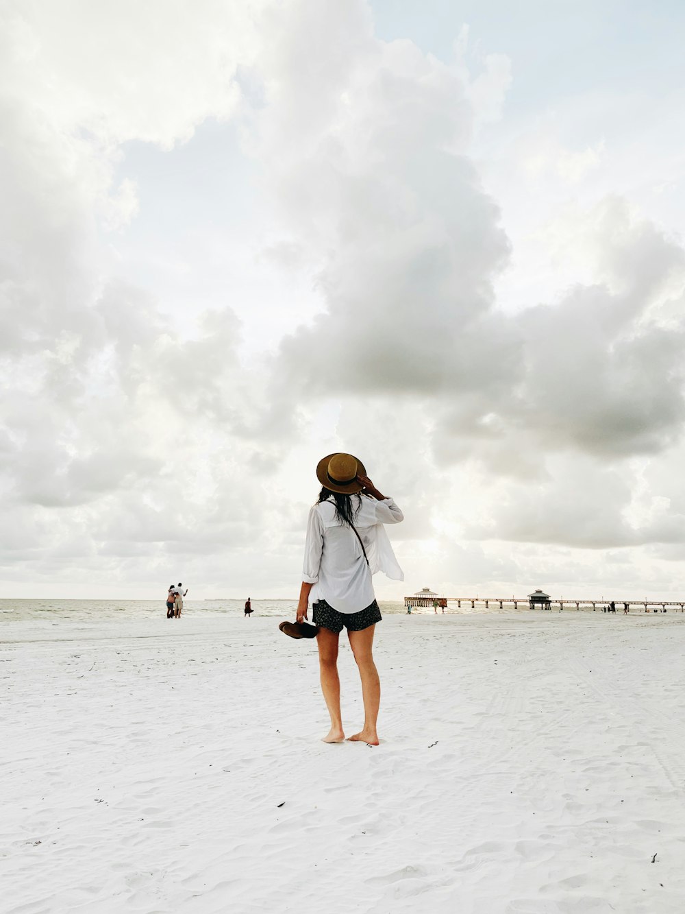mulher na camisa branca e shorts jeans azuis em pé na praia durante o dia