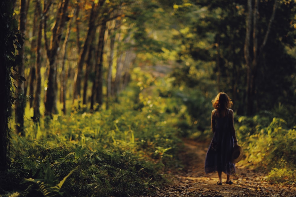 Frau in schwarzem Kleid, die tagsüber im Wald spazieren geht