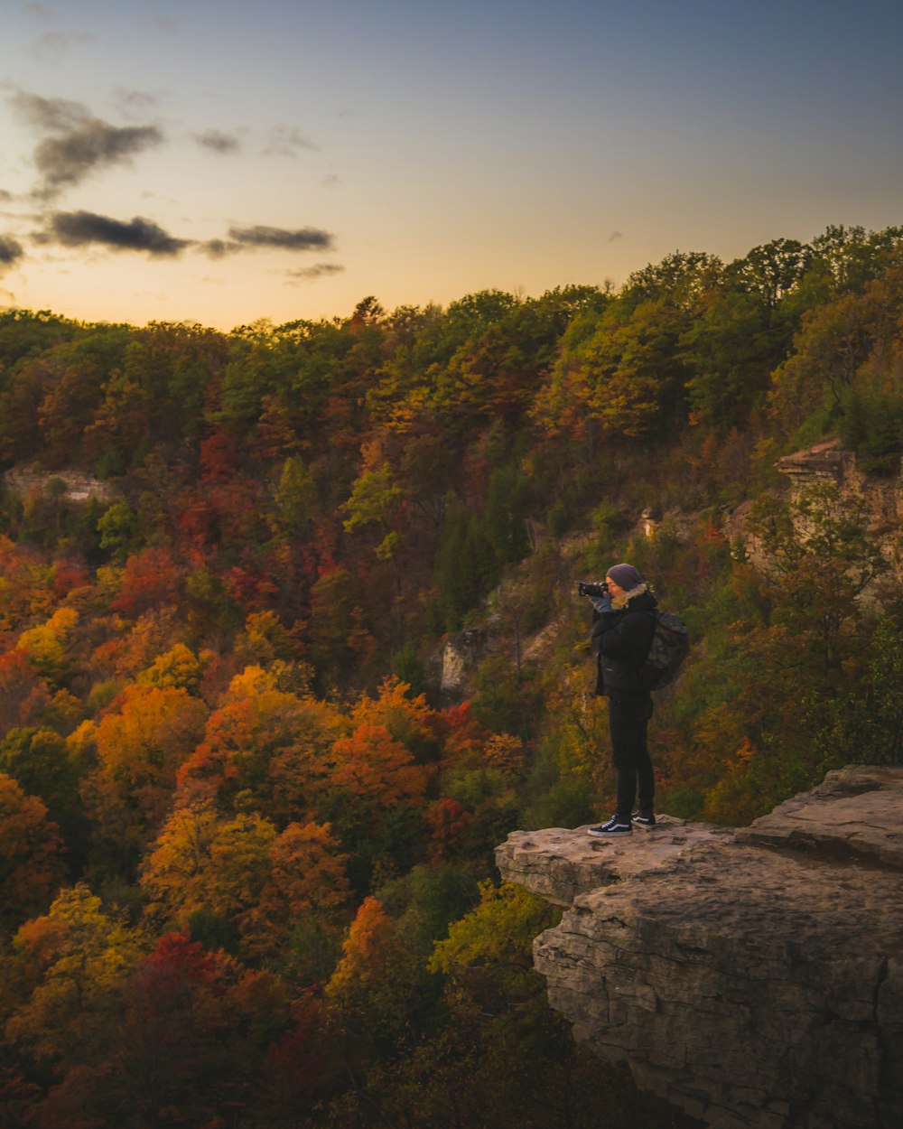 man in black jacket standing on rock near trees during daytime