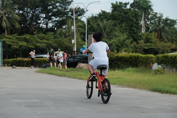 A parent watching their child ride a bike in a park.