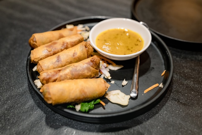 Golden crispy spring rolls arranged on a white ceramic plate with dipping sauce.