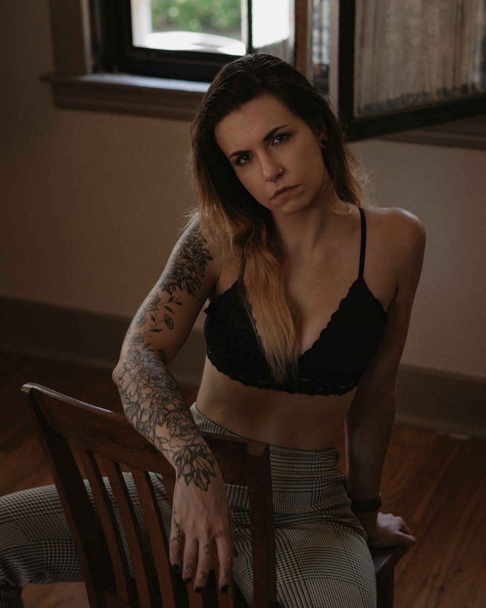 woman in black brassiere and gray pants sitting on brown wooden chair