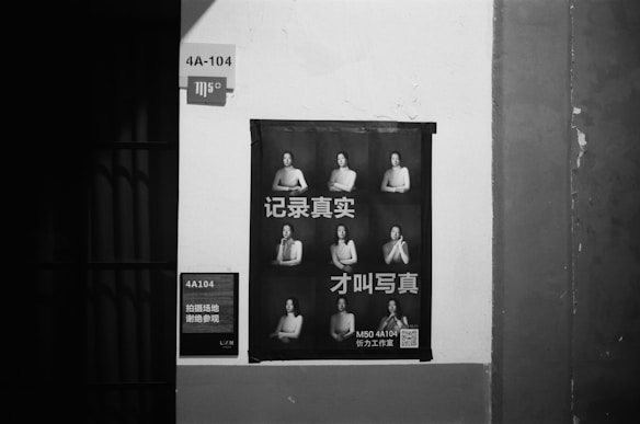 A monochrome poster is displayed on a wall, featuring nine images of a person in various poses. The poster includes Chinese text and is situated in an urban environment, likely indicating an exhibit or studio at location 4A-104.